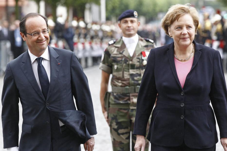 François Hollande und Angela Merkel schreiten an einem französischen Militärangehörigen vorbei.