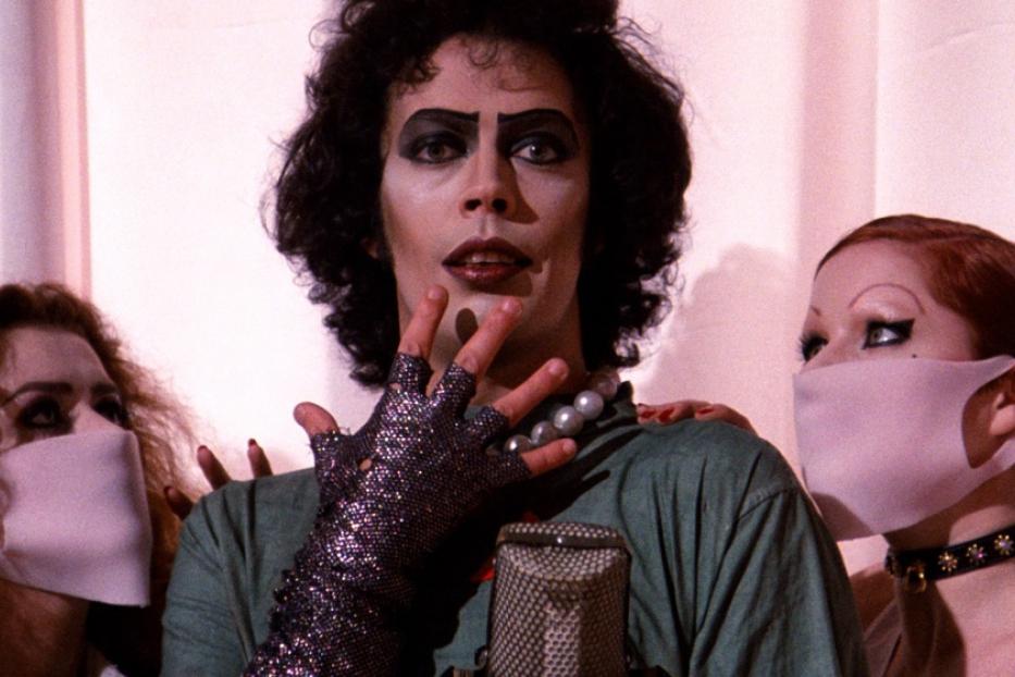 Frank N. Furter mit zwei maskierten Personen in einer Szene aus „The Rocky Horror Picture Show“.