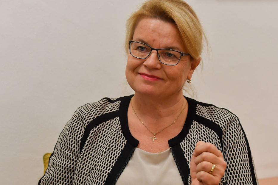 Eine blonde Frau mit Brille und Kreuzkette lächelt.