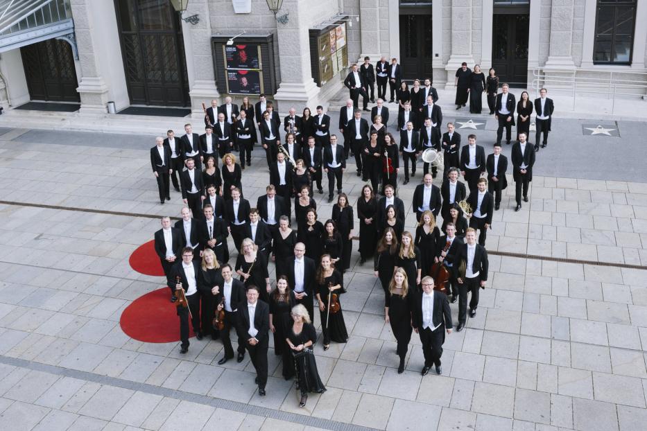 Ein großes Orchester steht vor einem Gebäude in Wien.
