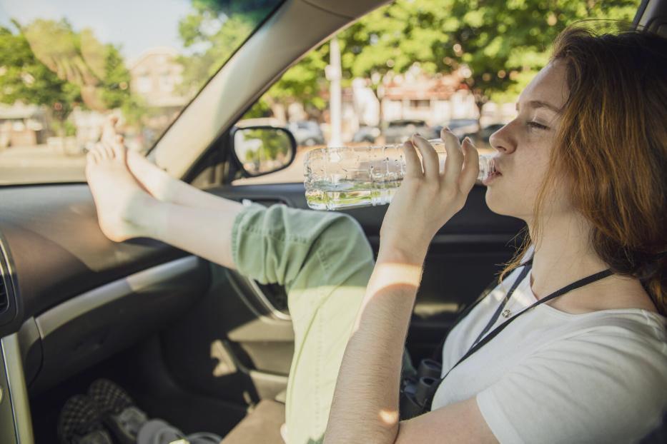 Teenager-Mädchen am Vordersitz eines Autos, barfuß die Füße auf der Amartur und aus einer Wasserflaschen trinkend