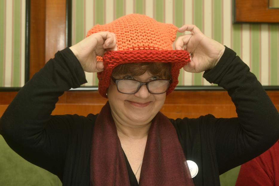 Eine Frau mit Brille setzt eine orangefarbene, gestrickte Mütze auf.