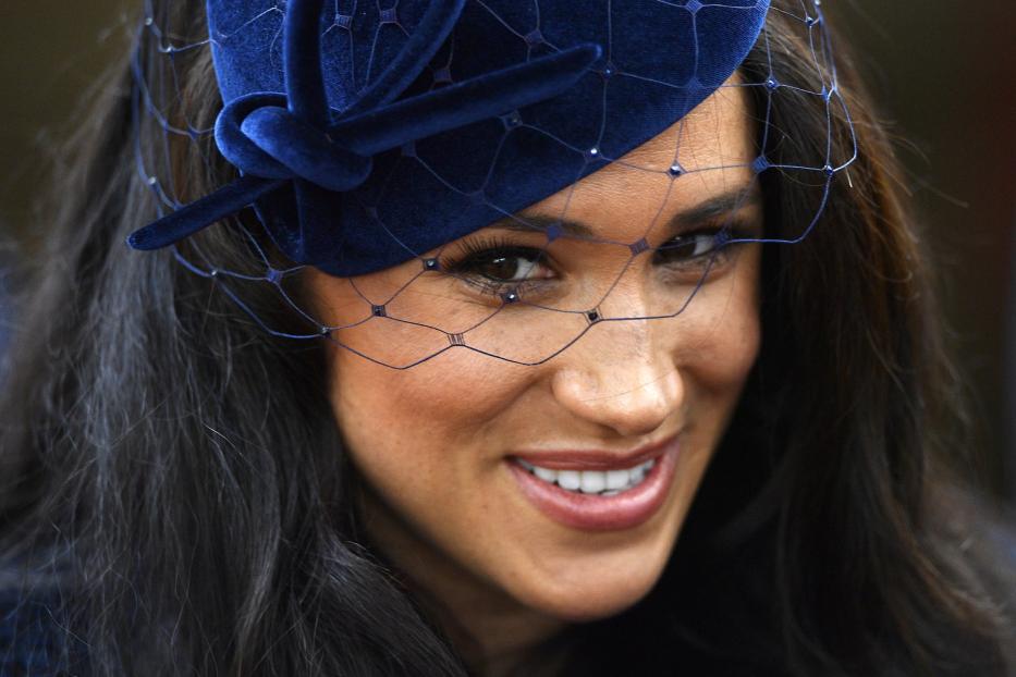 Meghan Markle mit einem blauen Hut und Schleier lächelt.
