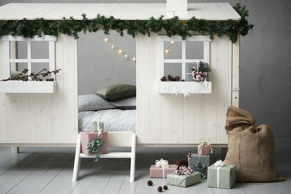 Ein weißes Kinderbett in Hausform ist weihnachtlich mit Geschenken und Tannengrün dekoriert.