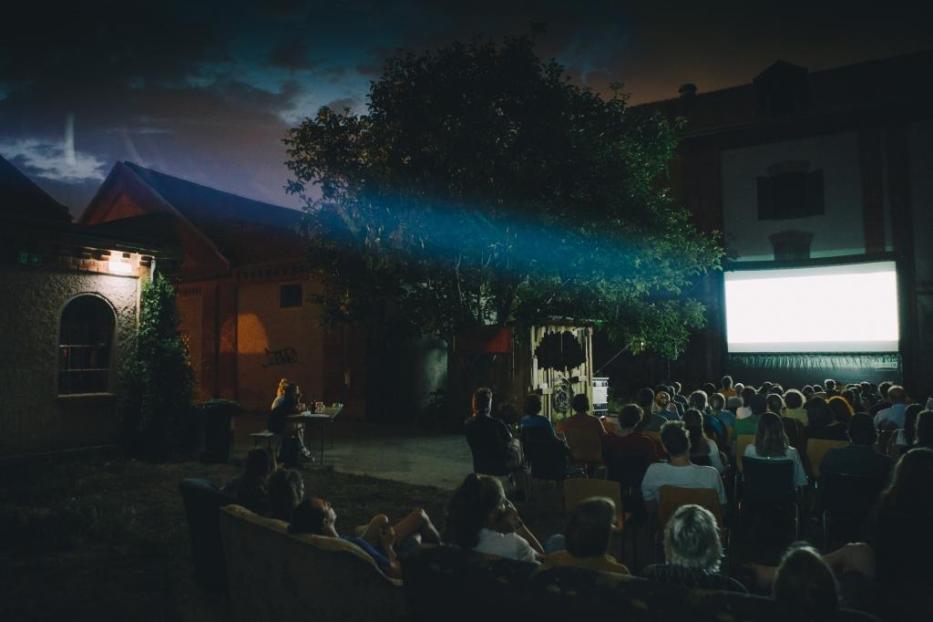 Zuschauer sitzen im Freien vor einer Leinwand für eine Filmvorführung.