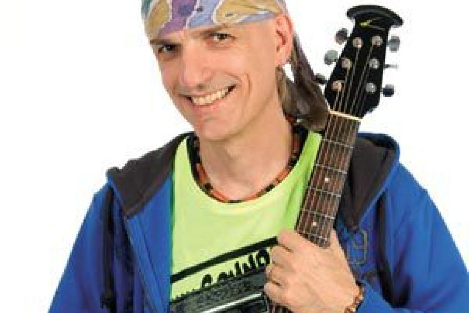 Ein Mann mit einem bunten Kopftuch lächelt und hält eine Gitarre.