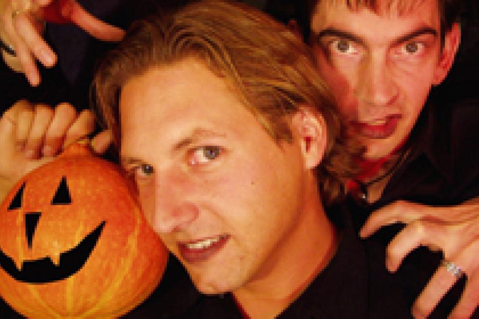 Ein Mann hält einen Kürbis, während andere als Vampire verkleidet hinter ihm stehen.