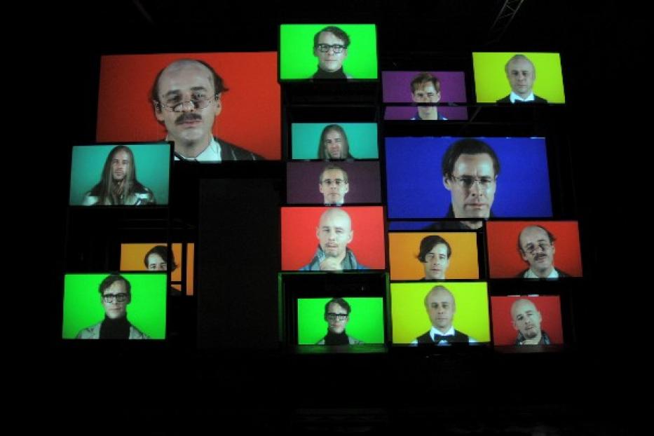 Eine Installation mit mehreren Bildschirmen, die Porträts von Personen zeigen.