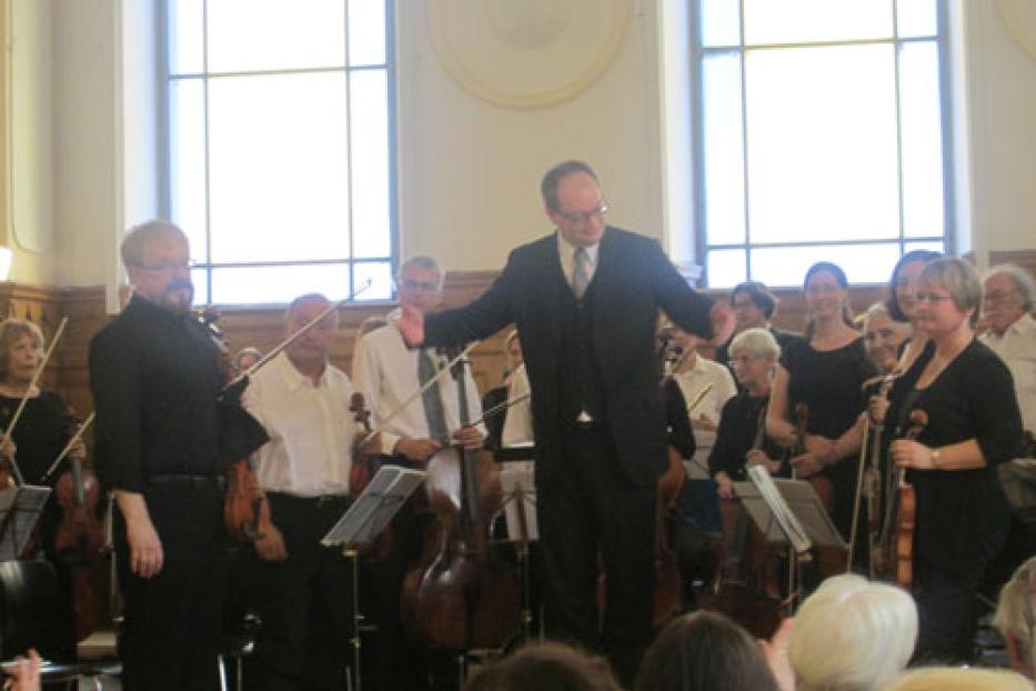 Ein Orchester mit Dirigent und Streichern spielt in einem Konzertsaal.