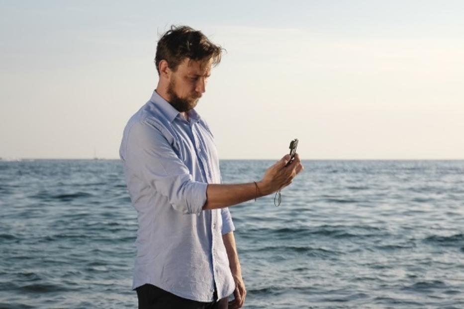 Ein Mann am Meer betrachtet einen Kompass.