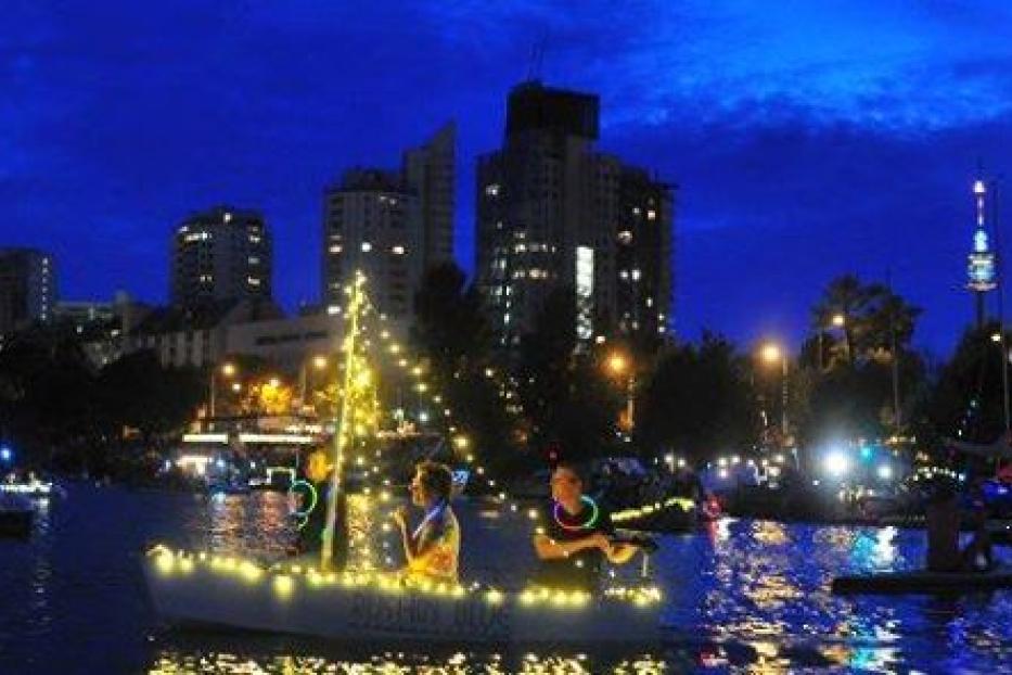 Ein mit Lichtern geschmücktes Boot fährt auf einem Fluss in Wien bei Nacht.