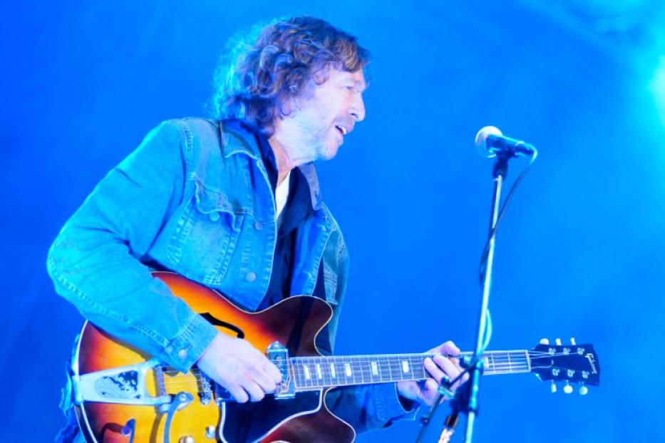Ein Mann mit Jeansjacke spielt Gitarre vor einem Mikrofon.