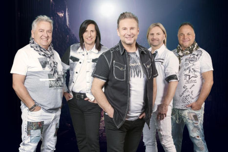 Das Nockalm Quintett posiert für ein Gruppenfoto vor einem dunklen Hintergrund.
