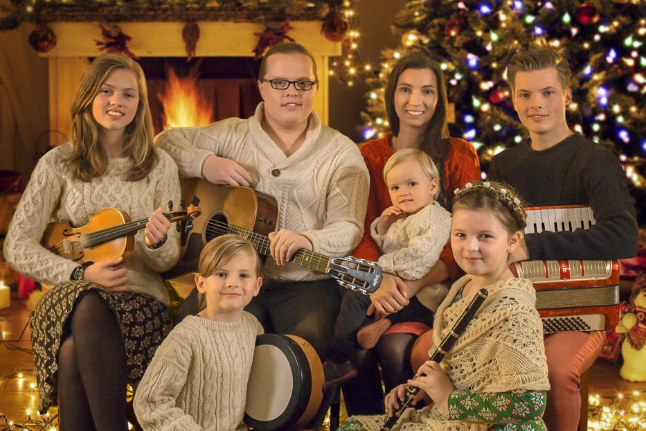 Eine Familie musiziert zu Weihnachten vor einem geschmückten Weihnachtsbaum und Kamin.