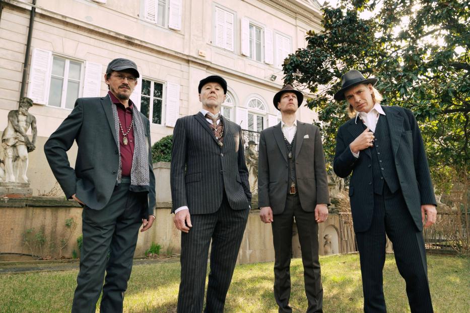 Die vier Musiker Ernst Molden, Willi Resetarits, Walther Soyka und Hannes Wirth posieren vor einem Gebäude.