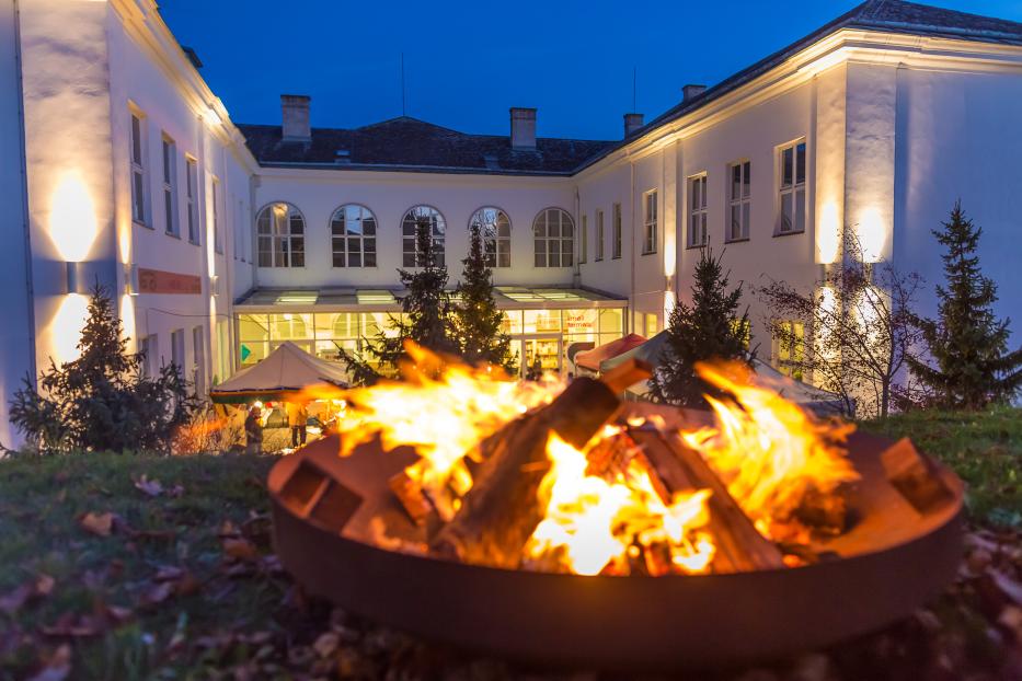 Ein Lagerfeuer brennt vor einem weißen Gebäude in Gugging.