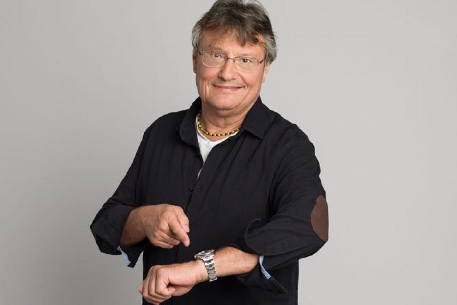 Joesi Prokopetz deutet auf seine Armbanduhr.