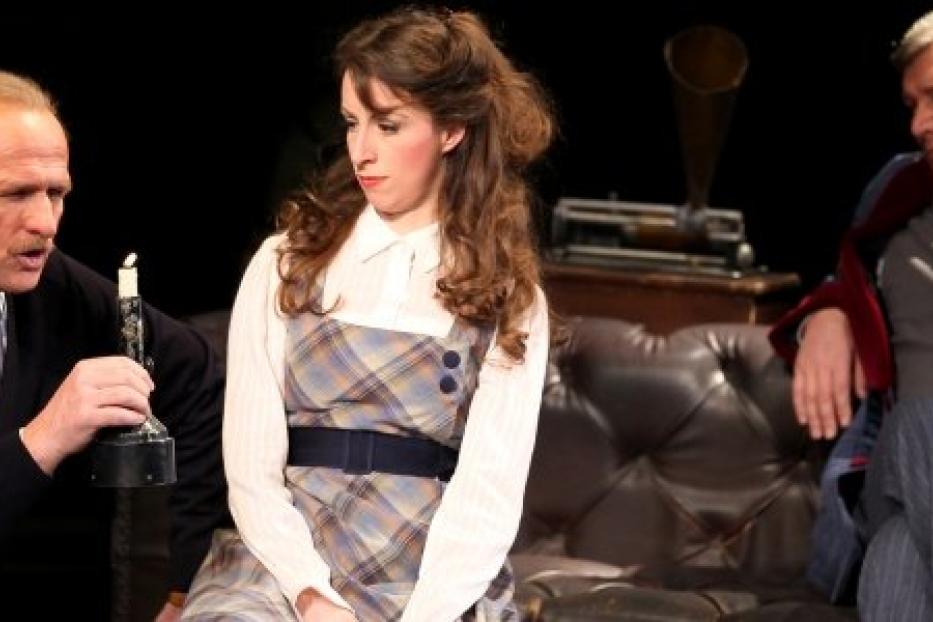 Szene aus einem Theaterstück mit drei Schauspielern auf einer Couch.