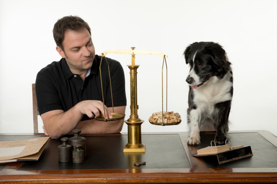 Martin Rütter und ein Border Collie an einer alten Waage mit Hundekuchen.