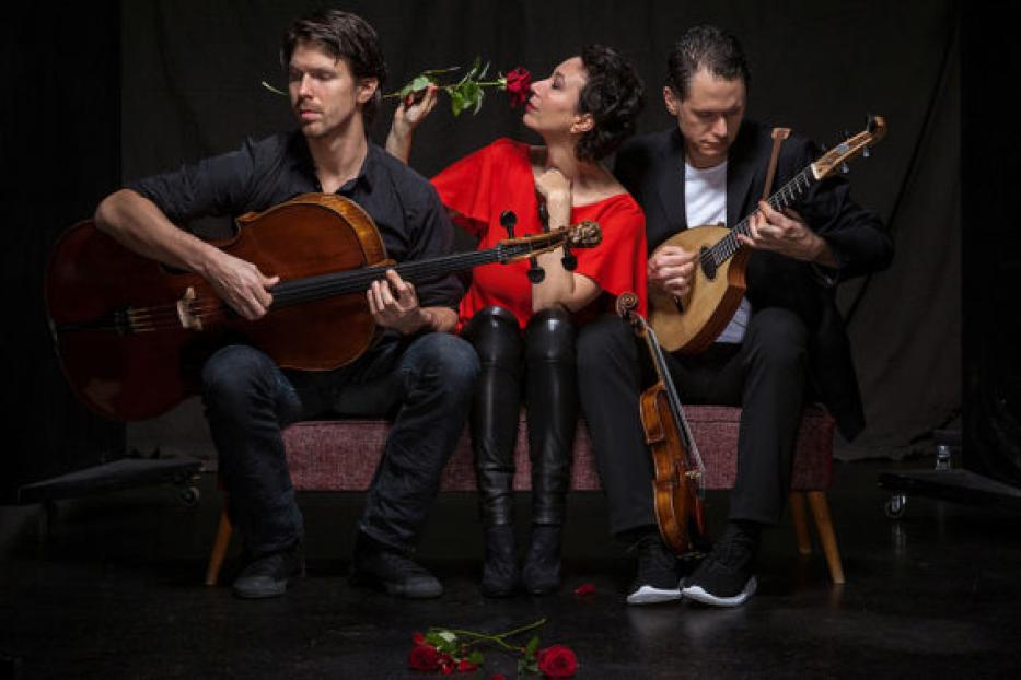 Drei Musiker sitzen mit Cello, Geige und Mandoline auf einer Bank.
