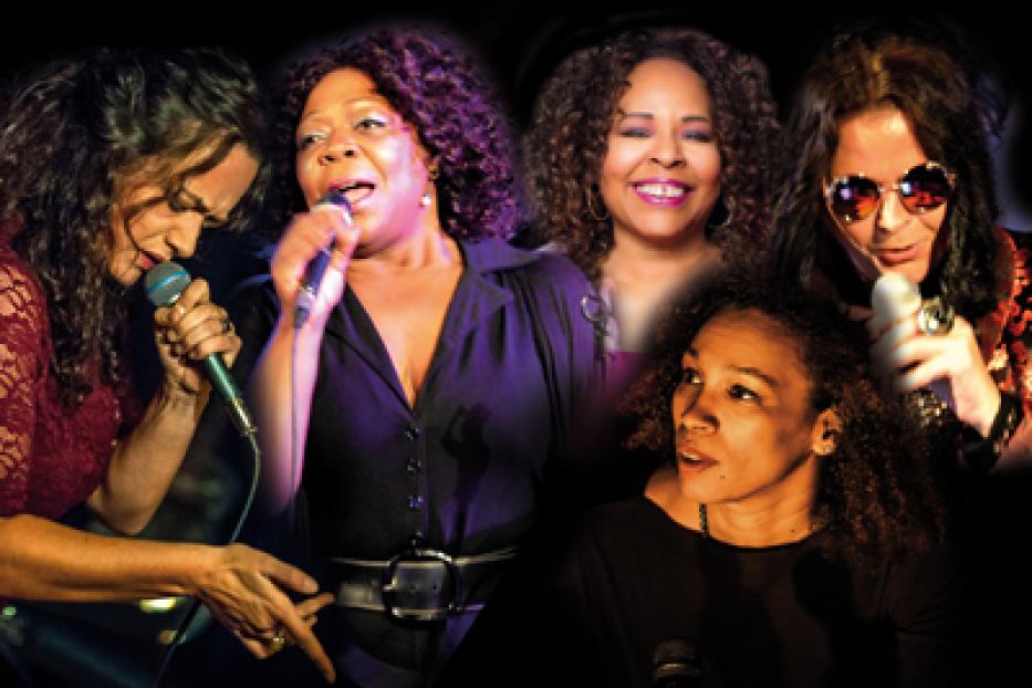 Fünf Frauen singen in einer Band ins Mikrofon.