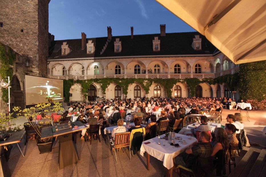 Ein Open-Air-Kino im Schlosshof mit vielen Zuschauern an Tischen.