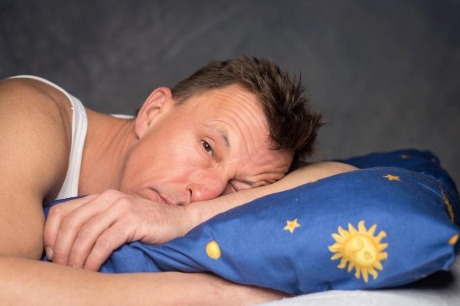 Ein Mann liegt müde auf einem blauen Kissen mit Sternen und Sonnen.