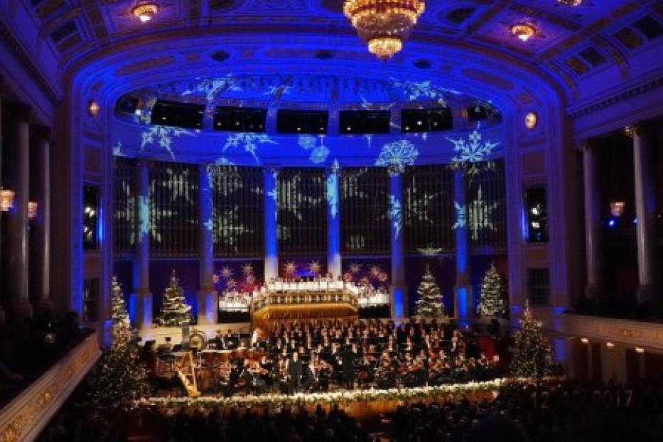 Ein Orchester und ein Chor treten in einem festlich geschmückten Konzertsaal auf.