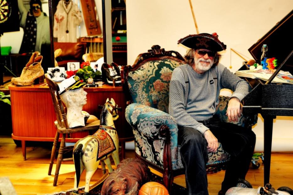 Helge Schneider sitzt mit Piratenhut und Sonnenbrille in einem dekorierten Sessel.