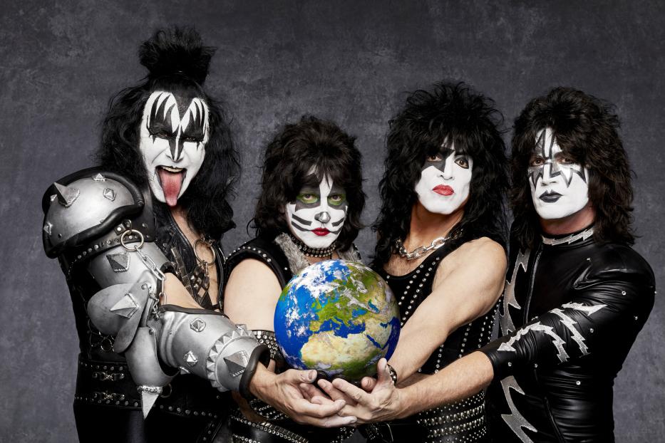Die Band Kiss mit Make-up und Kostümen hält eine Weltkugel.