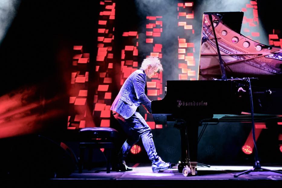 Ein Mann spielt ein schwarzes Bösendorfer Klavier auf einer Bühne mit roter Beleuchtung.