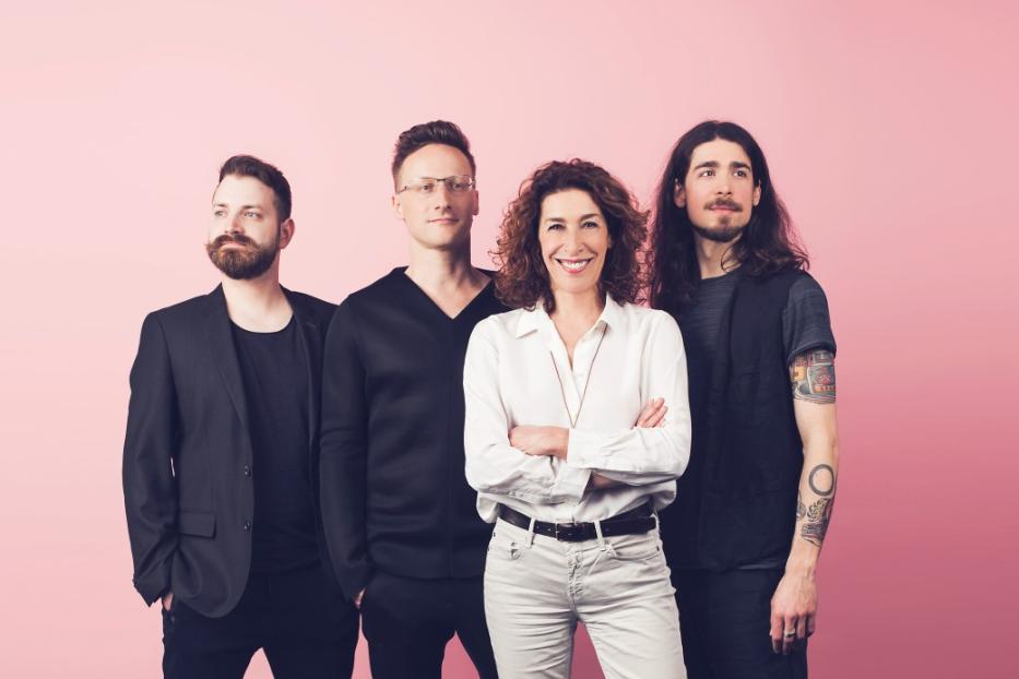 Die Schauspielerin Adele Neuhauser mit drei weiteren Personen vor einem rosa Hintergrund.