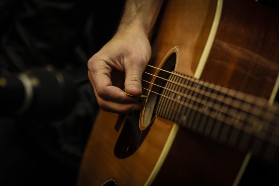 Eine Hand zupft mit einem Plektrum die Saiten einer Akustikgitarre.