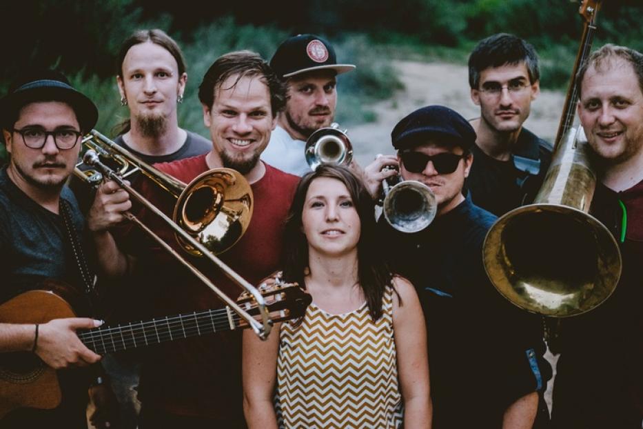 Eine Gruppe von acht Musikern mit Blasinstrumenten und einer Gitarre posiert für ein Foto.