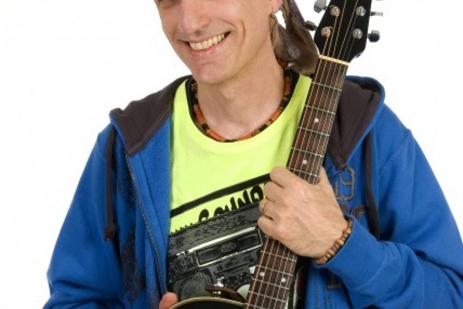 Ein lächelnder Mann mit einem bunten Tuch auf dem Kopf hält eine Gitarre.