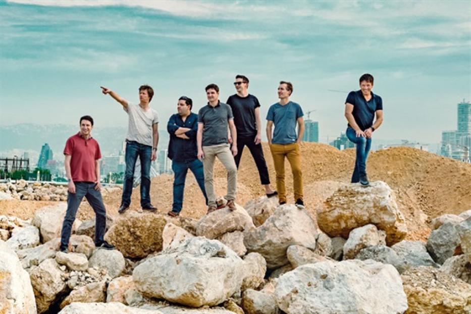 Die Gruppe Philharmonix steht auf einem Hügel mit Felsen vor einer Stadtkulisse.