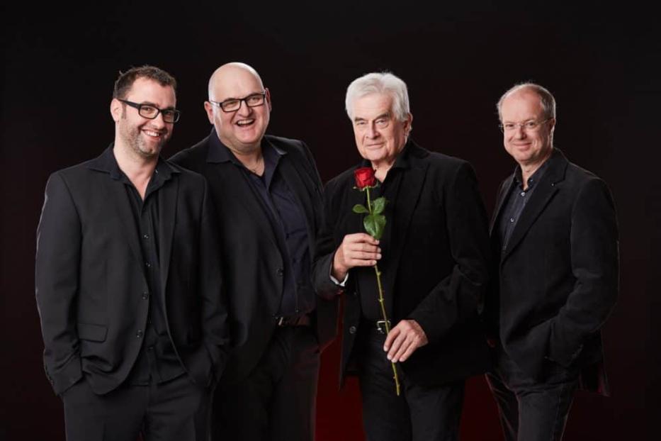 Die Band MG3 posiert mit Frank Hoffmann, wobei ein Mitglied eine rote Rose hält.