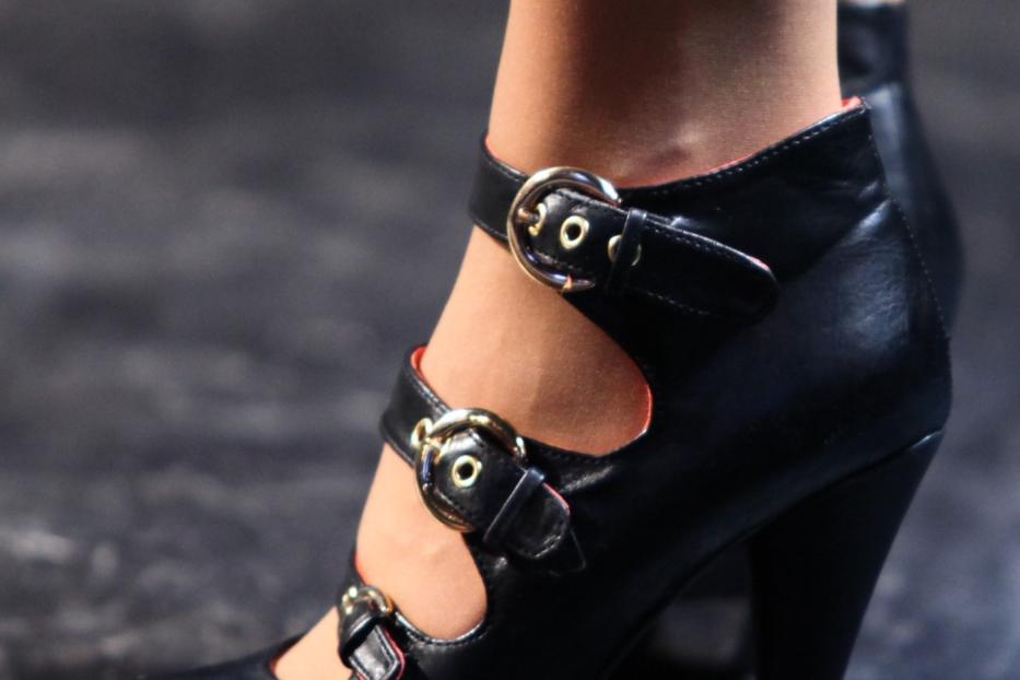 Nahaufnahme eines schwarzen High Heels mit Riemen und goldenen Schnallen.