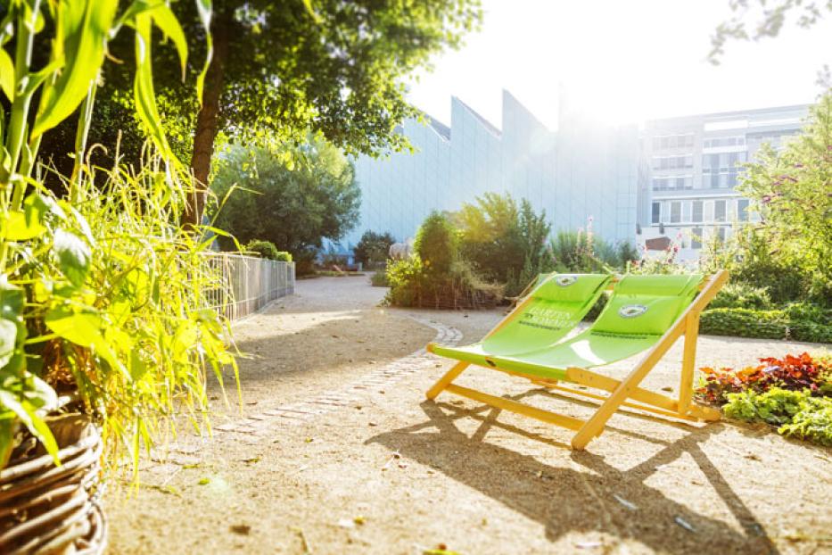 Zwei grüne Liegestühle im Garten vor einem modernen Gebäude.