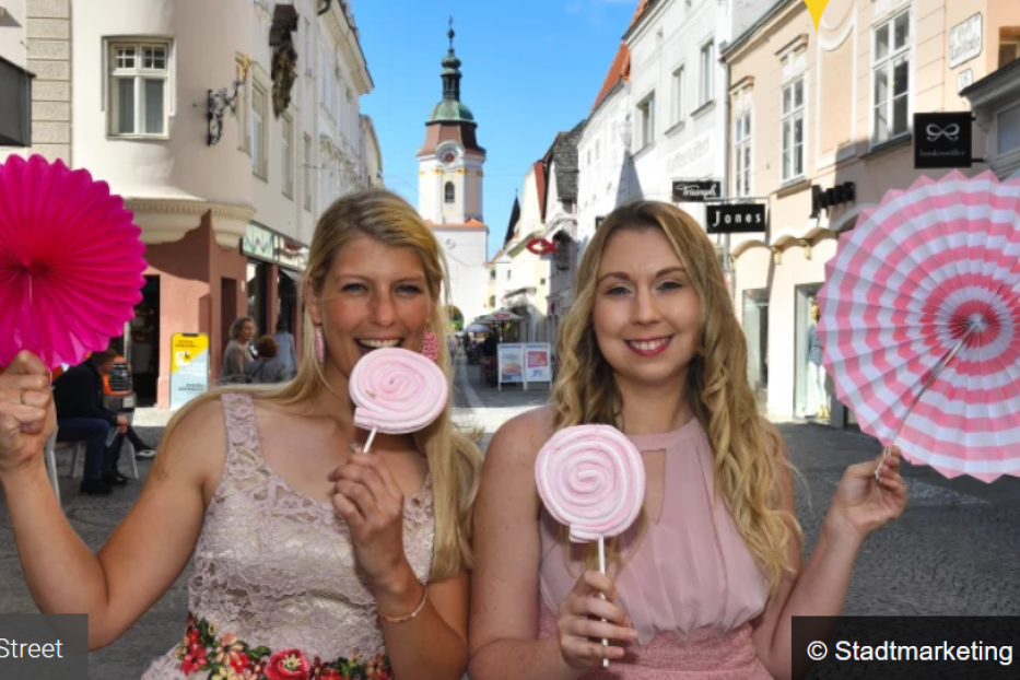 Zwei Frauen posieren mit Lollis und Papierfächern in der „Sweet Street“ in Krems.