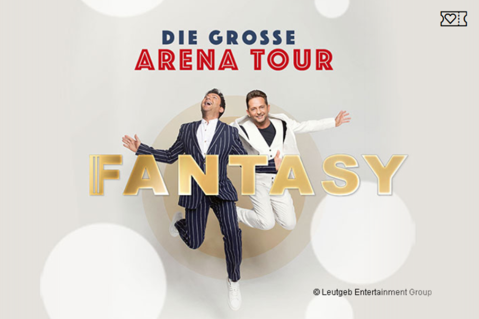 Das Schlagerduo Fantasy springt vor dem Schriftzug „Fantasy“ für ihre Arena Tour.