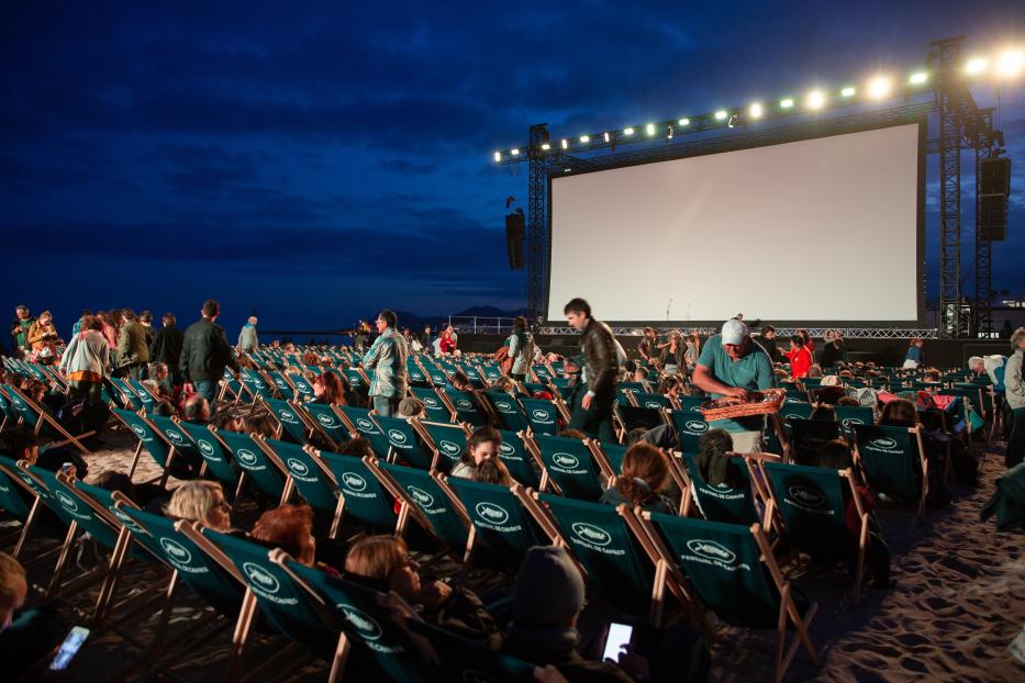 Zuschauer sitzen in Liegestühlen am Strand vor einer großen Leinwand beim Filmfestival in Cannes.