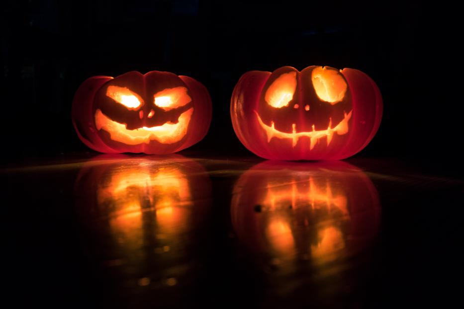 Zwei geschnitzte Halloween-Kürbisse stehen im Dunkeln und leuchten.