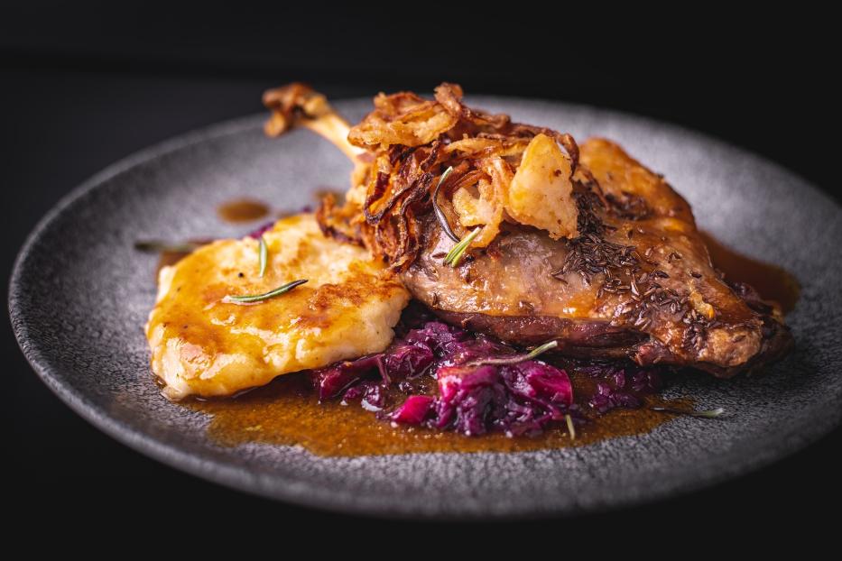 Gänsebraten mit karamelisierten Zwiebel, Knödel, Rotkraut und Bratensaft auf einem grauen Teller