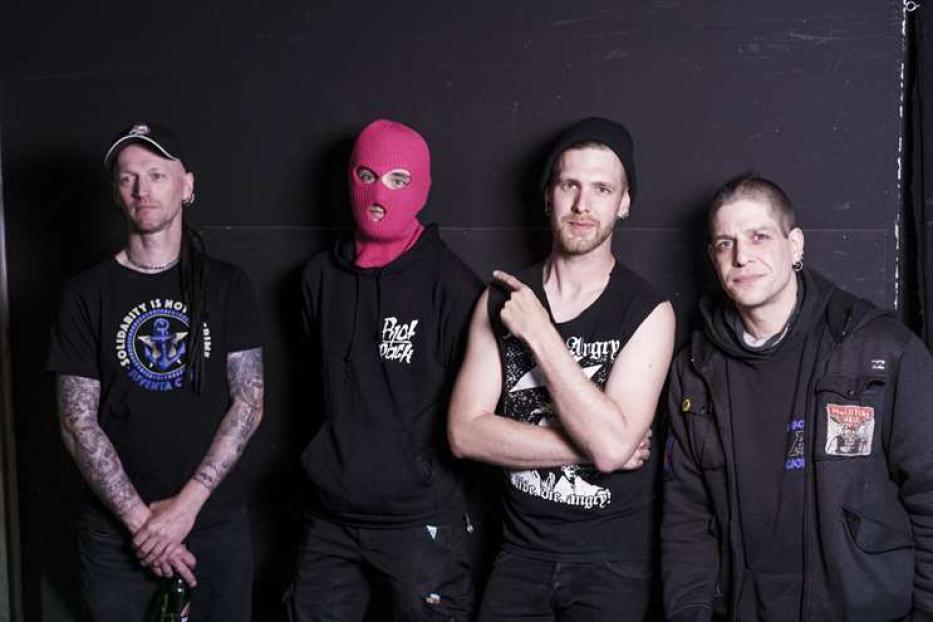 Eine Punkband posiert vor einer schwarzen Wand.