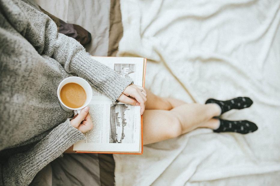 Ein Buch, eine Tasse Kaffee – auf dem Schoß einer Frau.