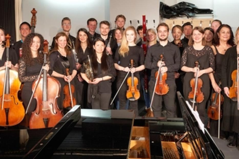 Ein Orchester mit Streichern, darunter Geigen und Celli, posiert für ein Gruppenfoto.