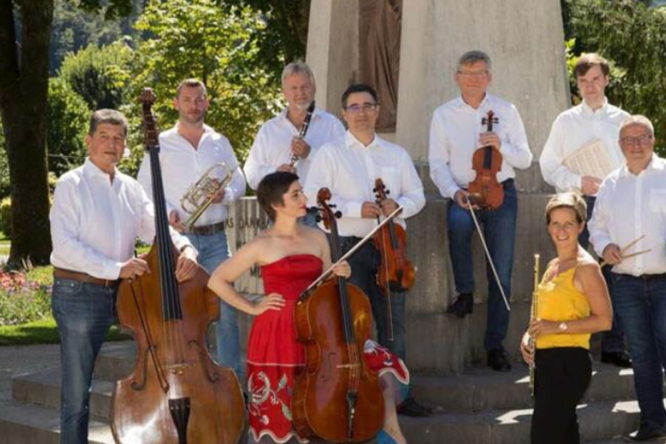 Ein neunköpfiges Orchester posiert mit ihren Instrumenten vor einem Denkmal.