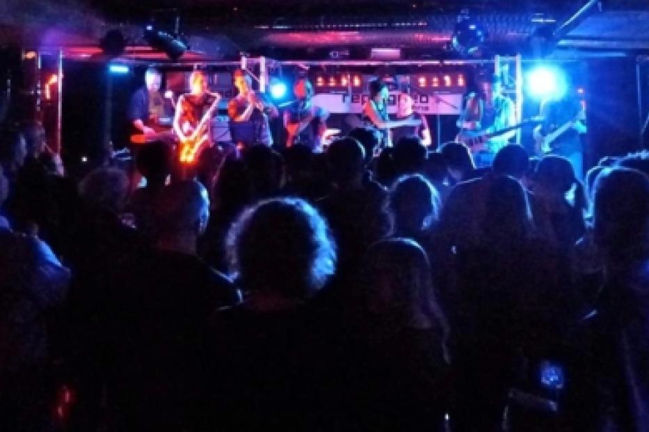Eine Band spielt vor Publikum auf einer Bühne mit blauer und roter Beleuchtung.