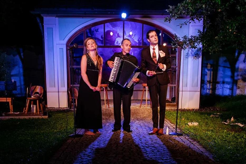Eine Musikgruppe tritt im Freien vor einem bemalten Fenster auf.